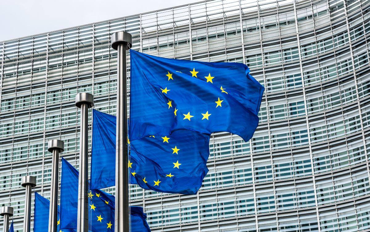 Bandiere dell’Unione Europea sventolano davanti alla facciata di un edificio moderno in vetro e metallo.