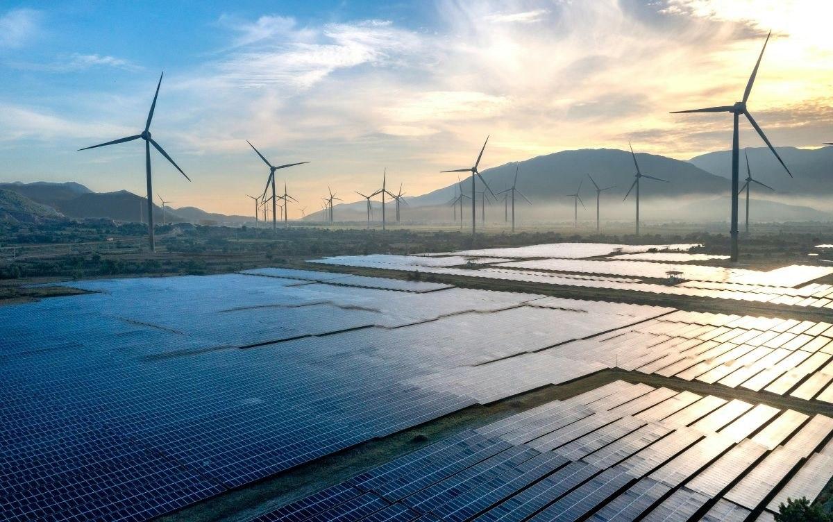 Parco fotovoltaico con pannelli solari in primo piano e turbine eoliche