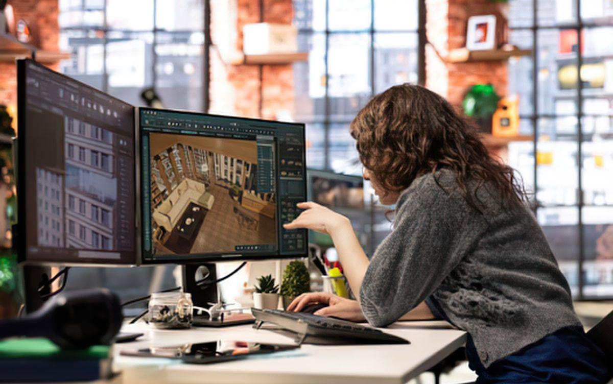 Una modellatrice 3D seduta alla scrivania davanti a due monitor mentre lavora al progetto digitale di un soggiorno con divano e arredi interni. Una modellatrice 3D seduta alla scrivania davanti a due monitor mentre lavora al progetto digitale di un soggiorno con divano e arredi interni.